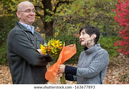 horizontal orientation of a man looking skeptical while a woman offers him flowers / Please Forgive Me!