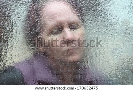 horizontal orientation close up of a sad looking woman behind a glass window which is covered in thick ice / The Long, Cold Winter of the Elderly