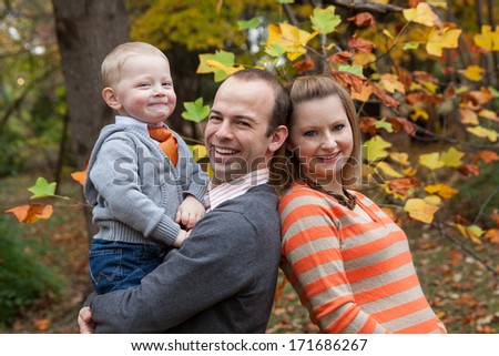 horizontal orientation of a happy, smiling, man, woman and child in the park with brightly colored trees (fall season) in the background / Fall Family Outing