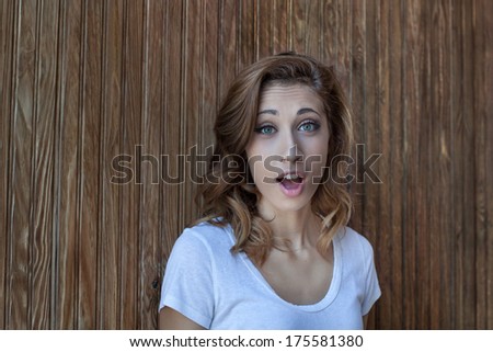 horizontal orientation close up of a young lady with a look of shock on her face with a wood background and copy space / I Don\'t Believe It!