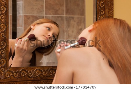 horizontal orientation close up of an older teenage girl applying powder to her chin line with a brush as she looks in the mirror / Correct Powder Application