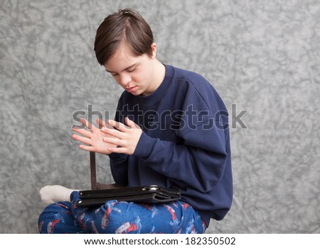 horizontal orientation of a boy with autism and down\'s syndrome clapping his hands as he plays with a tablet device / Apps for children with Autism