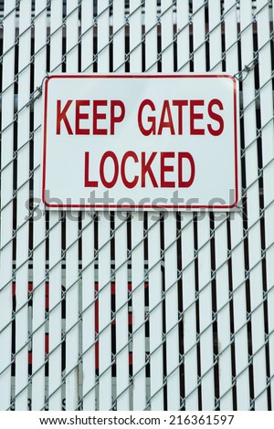 vertical orientation of a white fence with a generic sign that states KEEP GATES LOCKED and copy space / Keep Gates Locked Sign - Vertical