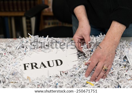 horizontal orientation close up of a woman\'s hands gathering shredded paper to recycle with the word FRAUD shown / Preventing Fraud