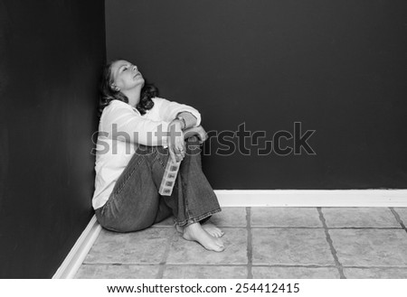horizontal orientation black and white image of an attractive, tired woman, in the corner of a dark room, with a pill box / Finding the right Medication
