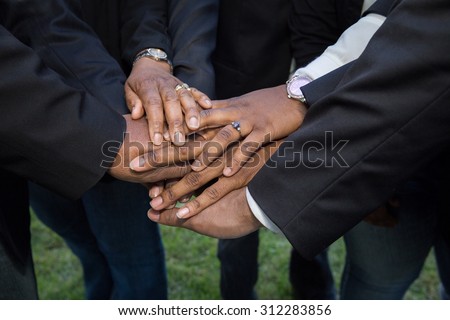 horizontal orientation close up of adult hands, wearing suits and business attire, stacked on one another in a show of unity and teamwork / Building Teamwork and Trust