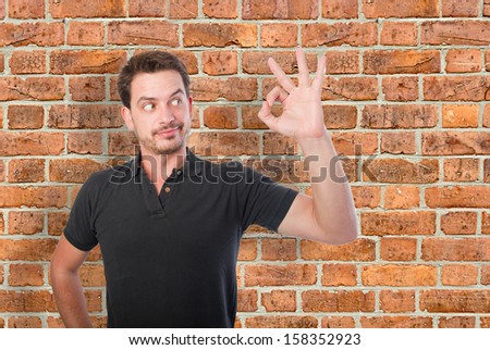 Young man doing a ok sign over a bricks wall