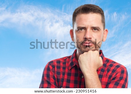 Young man with squares shirt over clouds background. Looking confident