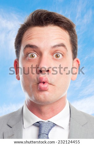 Young business man with grey suit over clouds background. Looking funny