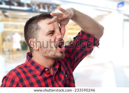 Man with red shirt over shopping center background. Grabbing his nose