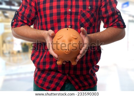 Man with red shirt over shopping center background. Holding a piggy bank