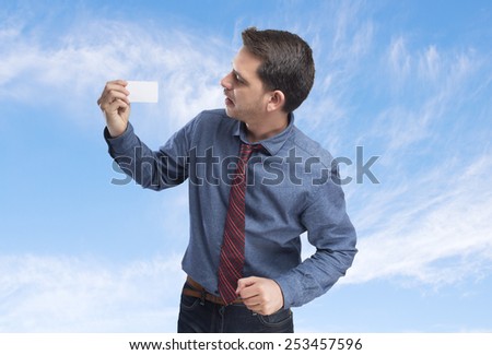 Man wearing a blue shirt and red tie. He is holding a white card. Over clouds background