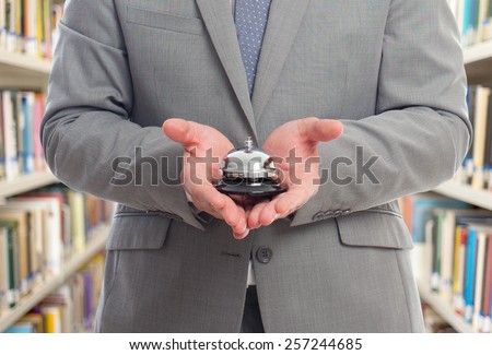 Business man with grey suit holding a hotel bell. Over library background