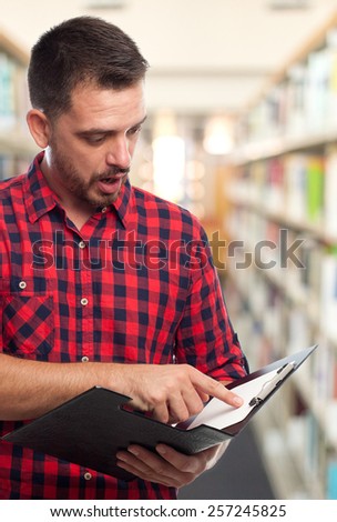 Man with red squares shirt. He looks surprised into a black folder. Over library background
