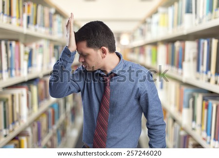 Man wearing a blue shirt and red tie. He looks upset. Over library background