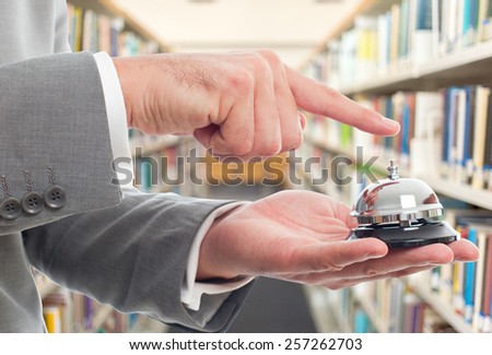 Business man with grey suit. He is using hotel bell. Over library background
