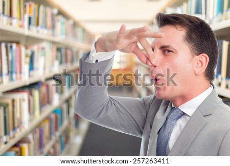 Business man with grey suit, He is upset because of a smell. Over library background