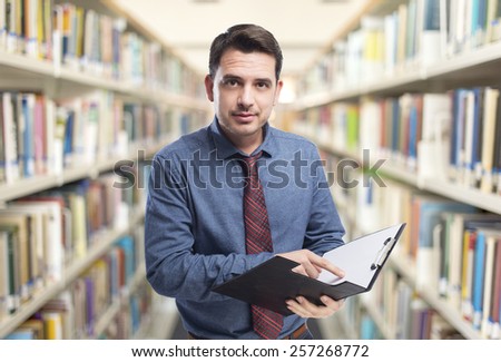 Man wearing a blue shirt and red tie. He is holding a black folder. Over library background