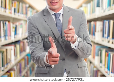 Business man with grey suit. He is pointing with his fingers. Over library background