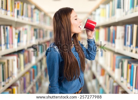 Trendy young woman drinking from a red cup. Over library background