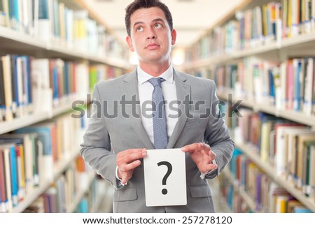Business man with grey suit holding a question mark. Over library background