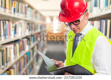 Architect man wearing a red helmet and reading from a black folder. Over library background