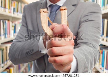 Business man with slingshot. Over library background