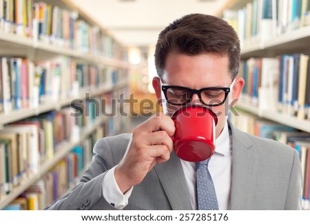 Business man with grey suit. He is drinking from a red cup. Over library background