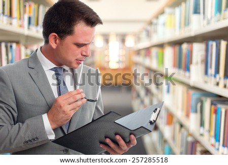 Business man with grey suit reading from a black folder. Over library background