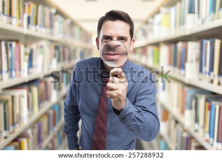 Man wearing a blue shirt and red tie. He is holding a magnifying glass. Over library background