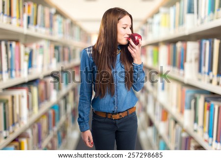 Trendy young woman smelling a red apple. Over library background