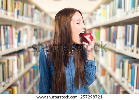 Trendy young woman eating a red apple. Over library background