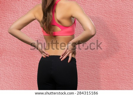 Young woman wearing a gym clothes. She has a back ache. Over red background