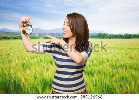 Smiling woman pointing to a clock with her finger. Over meadow background