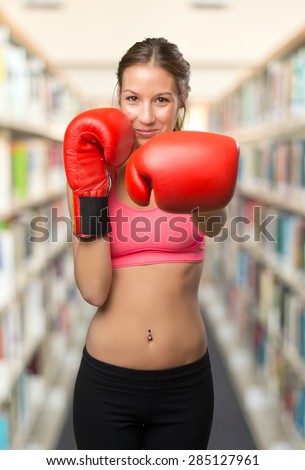 Young woman wearing gym clothes. She is ready to fight with her boxing gloves. Over library background