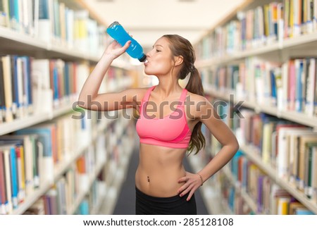 Young woman with fitness look drinking water. Over library background
