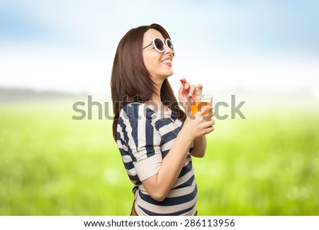 Smiling woman with white sunglasses drinking a juice. Over nature bokeh background