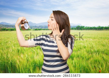 Quirky woman looking to a clock. Over meadow background