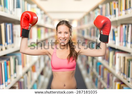 Young woman wearing boxing gloves. She looks happy. Over library background