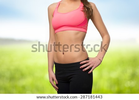 Young woman wearing gym clothes. Her belly closeup. Over nature background