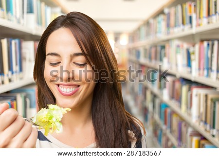 Smiling woman eating a salad. Over library background