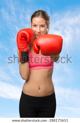 Young woman wearing gym clothes. She is ready to fight with her boxing gloves. Over clouds background