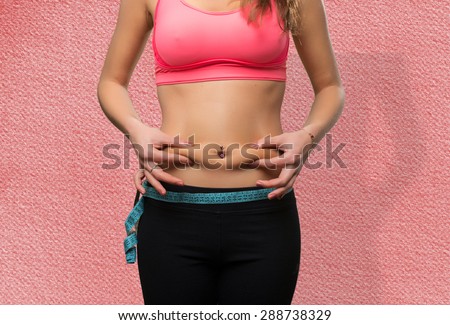Young woman belly close up with a measurement scale. She is grabbing her fat. Over red background