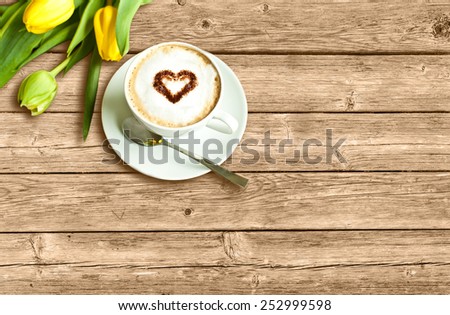 Cup of coffee with heart and yellow tulips on the wooden background
