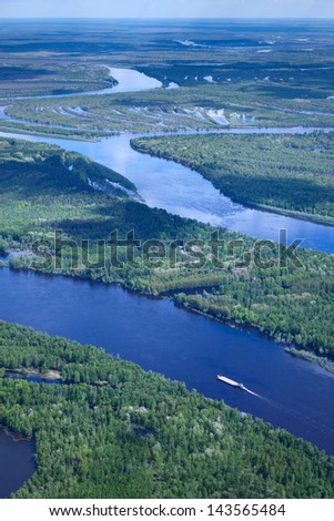 Aerial view of forest the river during summer day. The ship with barge moves along the river.