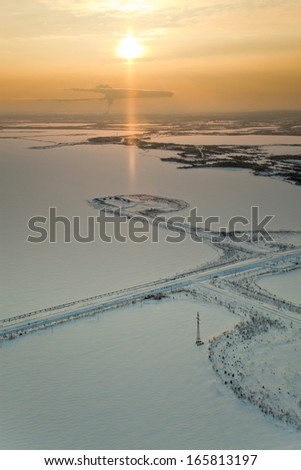 Aerial view of the frozen lake on which are made petroleum production. Roads were run directly through the lake. High clouds bright are lighted by morning sun.