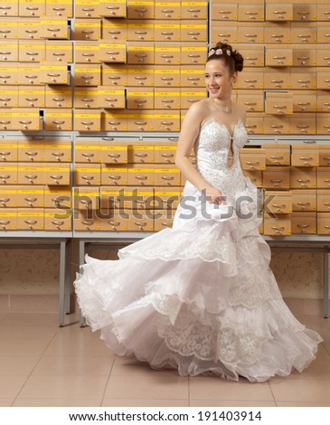 There is a bride standing in front of big cupboard-catalog. It is bank of data which contain information about the probable grooms.