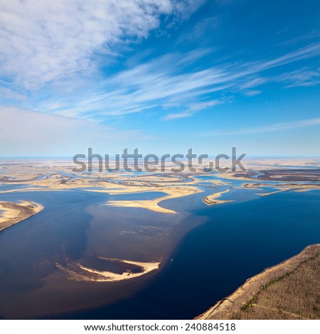 Aerial view over flood-land beside great river during spring. Great plain is divided into many parts by a lot of number of rivers and channels. Water meadows are covered by yellow last year\'s grass.