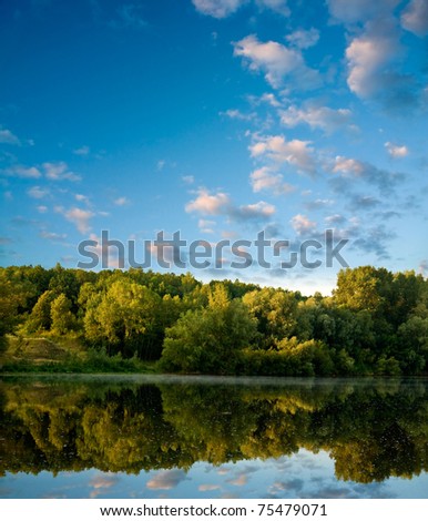 Summer landscape with river and pink clouds on blue sky.