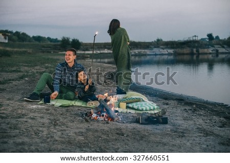 Happy young family sitting around the campfire on the beach at night fall, mother, father, son